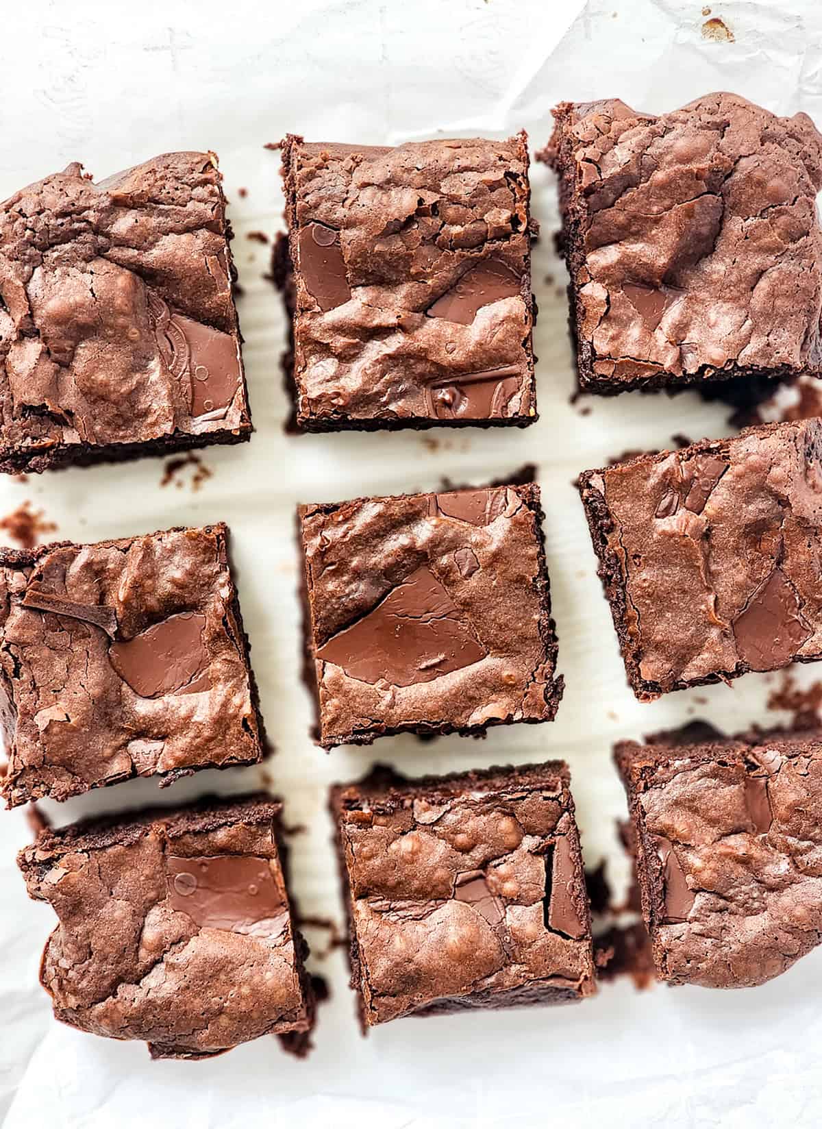 Nine chocolate brownies, made from a rich condensed milk brownie recipe, are arranged in a grid on parchment paper, displaying cracked tops and chocolate chunks.