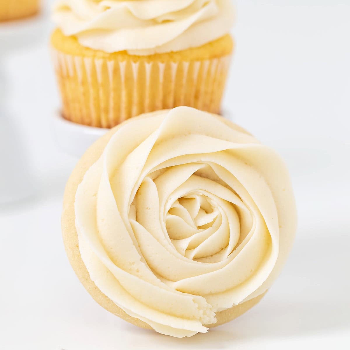 Cupcake with a swirl of white vanilla frosting piped in the shape of a rose, with another cupcake in the background.