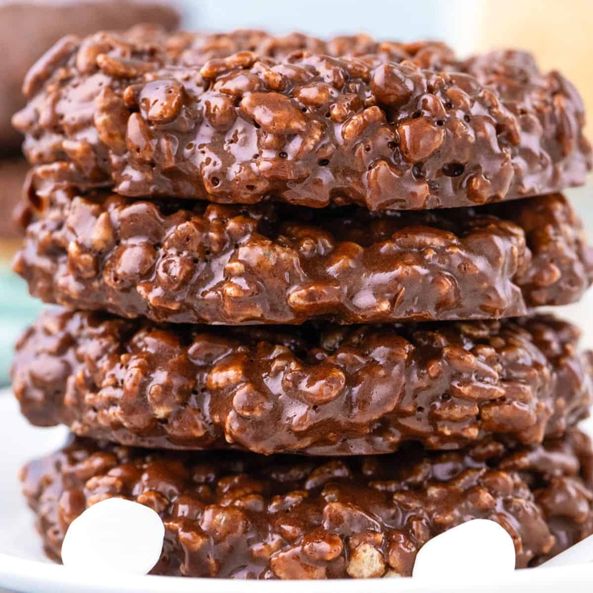 A stack of four chocolate no-bake cookies, reminiscent of classic Star Crunch Cookies, with a textured, glossy surface, shown close-up on a white plate.