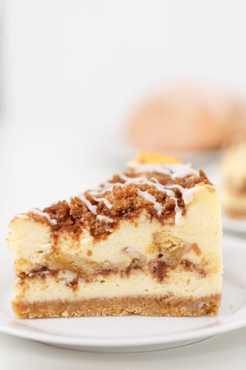 A slice of Honey Bun Cheesecake with a crumbly streusel topping and icing drizzle, served on a white plate.
