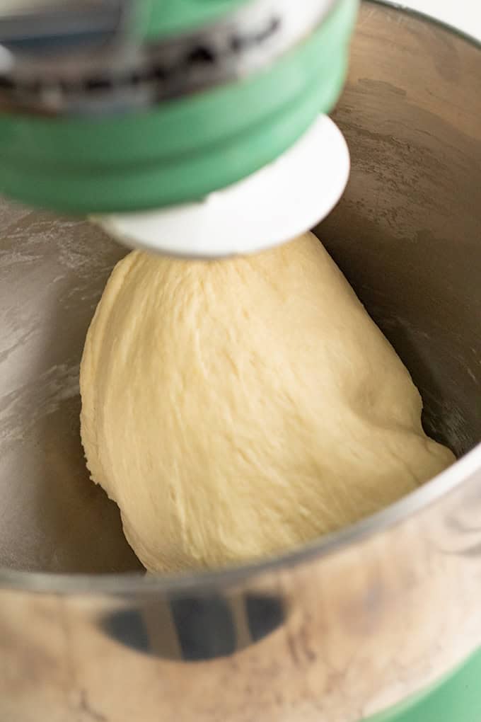 A stand mixer is kneading a ball of dough in a metal mixing bowl, preparing it for delicious chocolate chip cinnamon rolls.