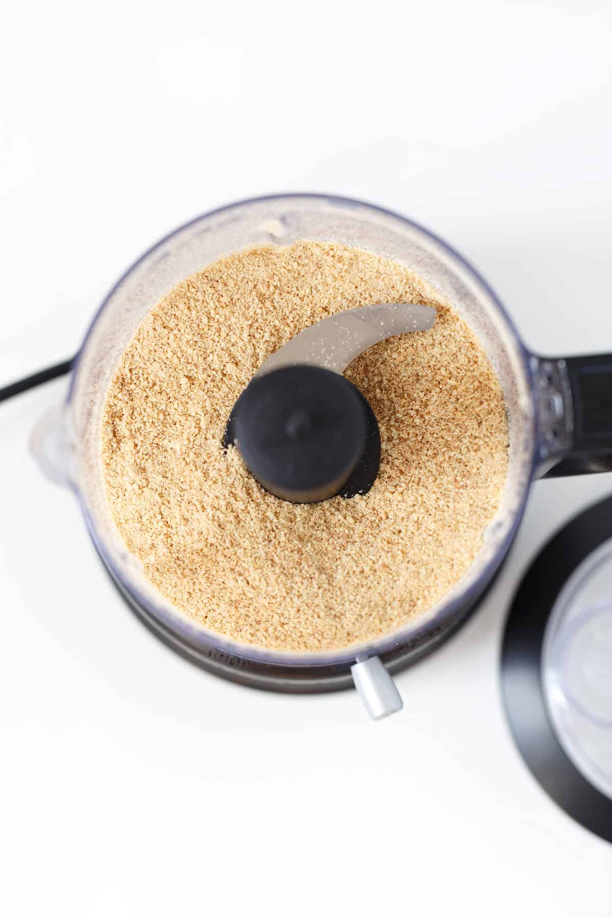 A food processor bowl filled with finely ground Graham Cracker crumbs, viewed from above, perfect for a delicious crust recipe.