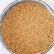 A round cake pan lined with parchment paper is filled with an even layer of homemade graham cracker crust, perfect as a base for your favorite pie crust or graham cracker crust recipe.
