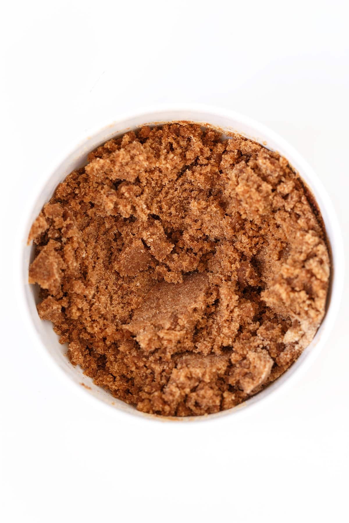 A close-up top view of a white bowl filled with brown sugar, showing a coarse and slightly clumped texture—perfect for adding sweetness to a honey bun or cheesecake recipe.