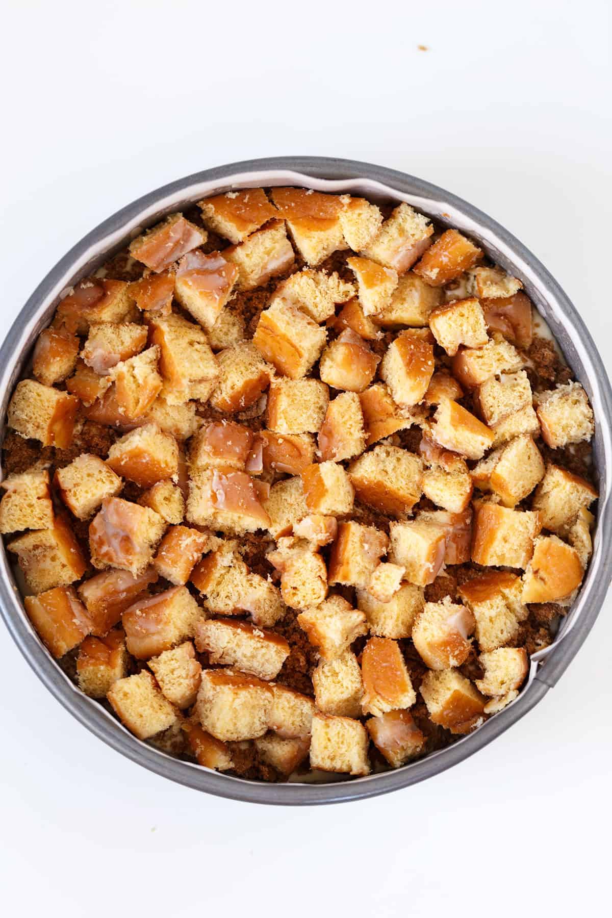 A round baking pan filled with cubed pieces of glazed Honey Bun Cheesecake, arranged in an even layer.