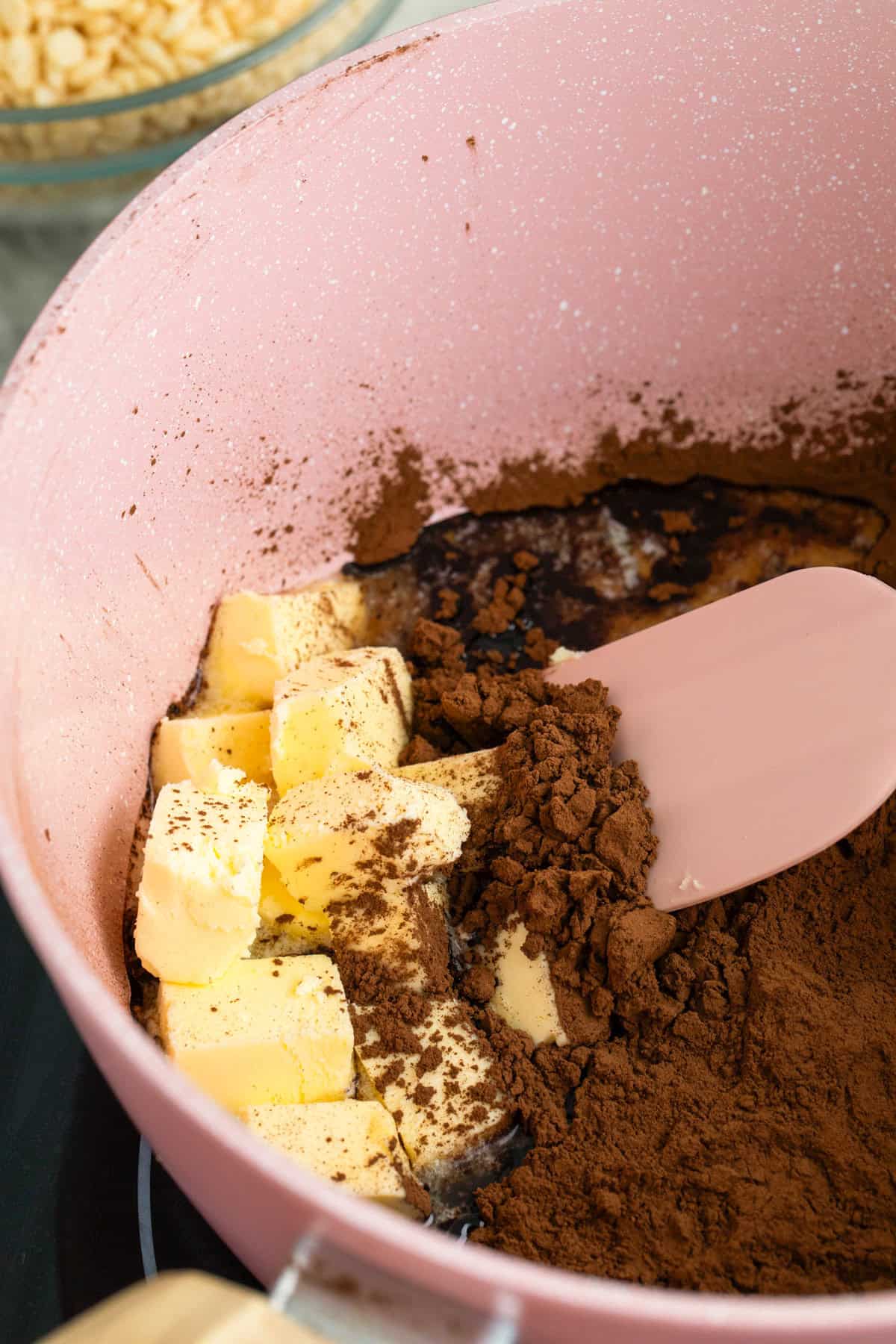 Butter and cocoa powder being mixed with a pink spatula in a pink saucepan, creating the rich chocolate base for delicious Star Crunch Cookies.