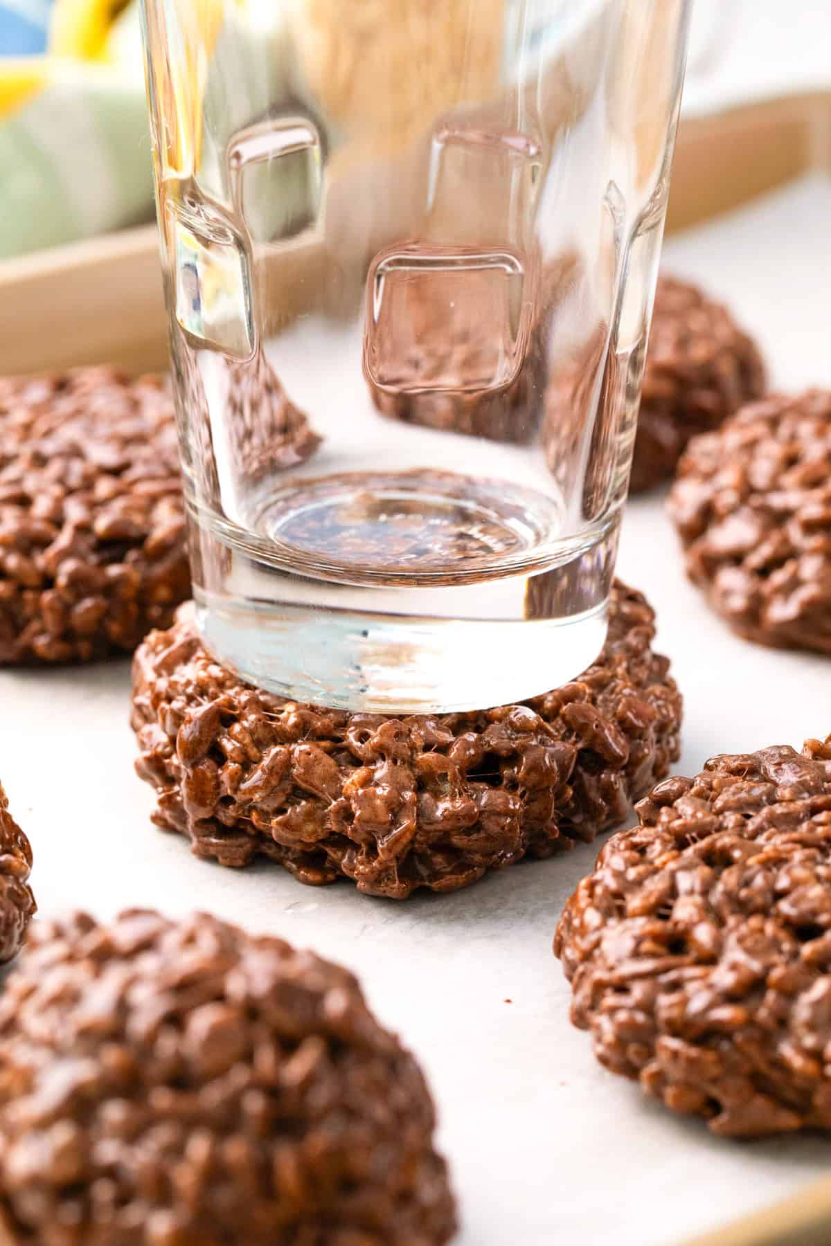 A glass is being used to flatten a Star Crunch Cookie on a parchment-lined baking sheet, with more chocolate crispy rice cookies nearby.
