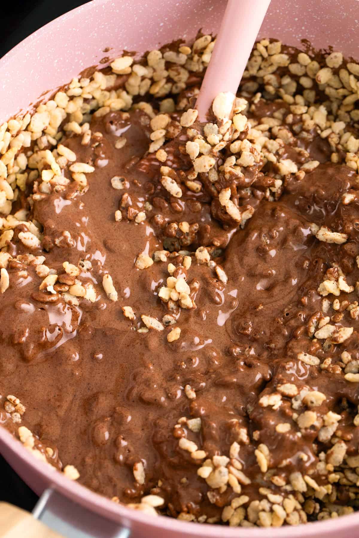 A close-up of a pink mixing bowl with a spatula stirring chocolate-coated puffed rice cereal, perfect for making homemade Star Crunch snack cookies.