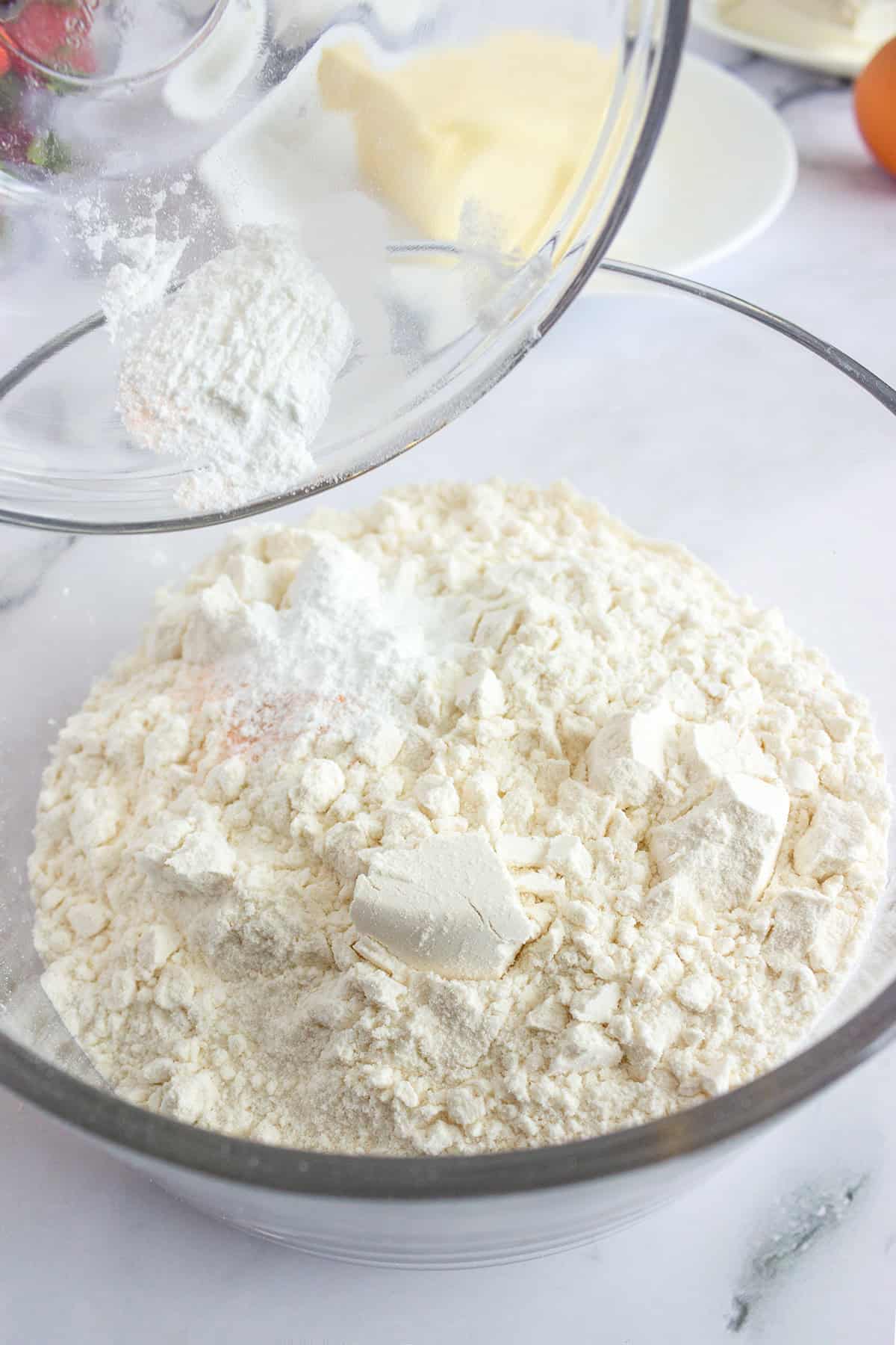 A glass bowl of flour with chunks of butter being added from another bowl, set on a marble countertop&mdash;perfect for making a delicious Strawberry Dessert like classic Strawberry Pizza.