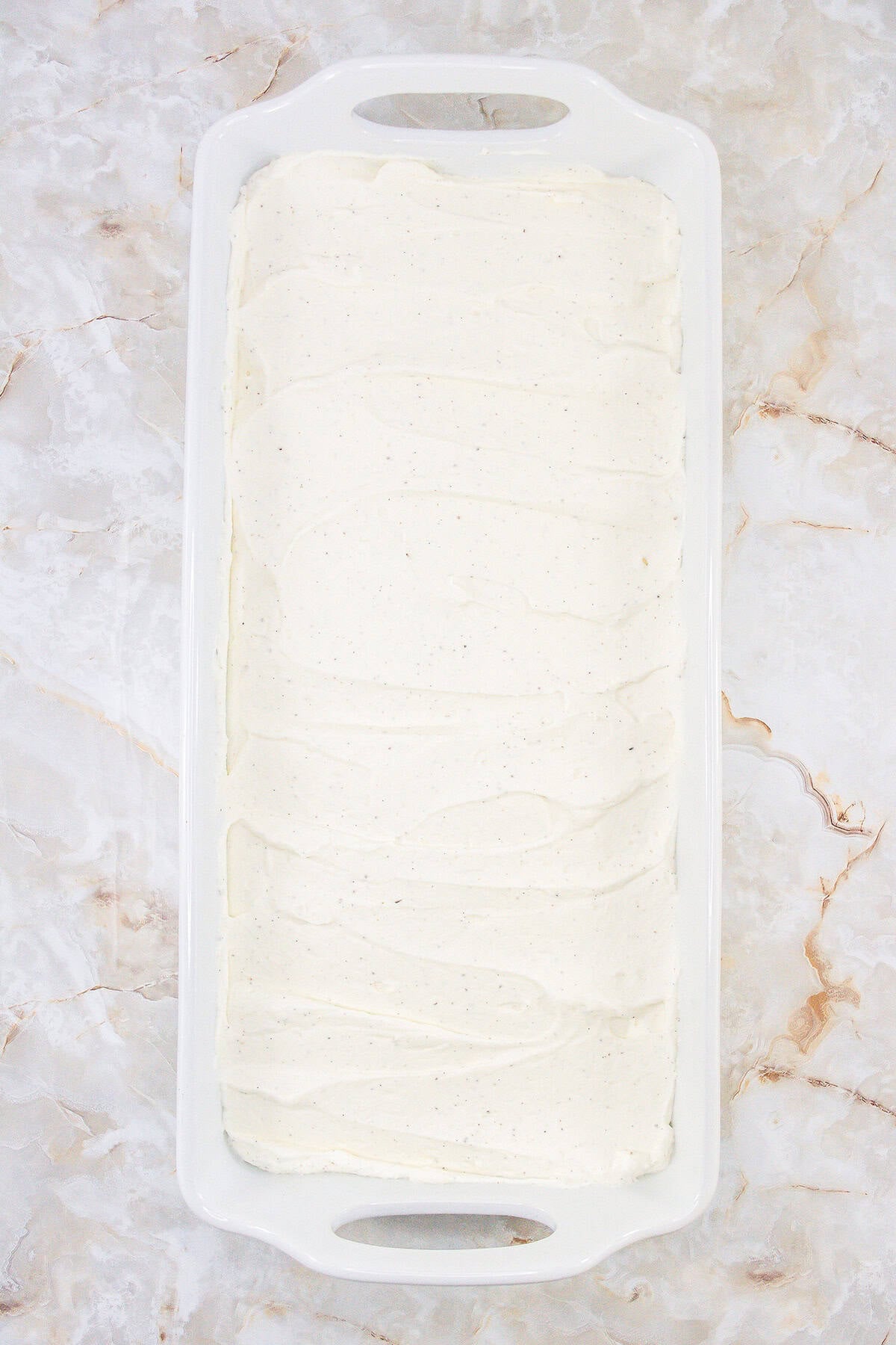 A rectangular white dish filled with a smooth layer of vanilla ice cream, crafted using a no churn method, sits elegantly on a marble surface.
