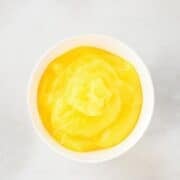 A white bowl filled with smooth yellow custard on a light gray surface.