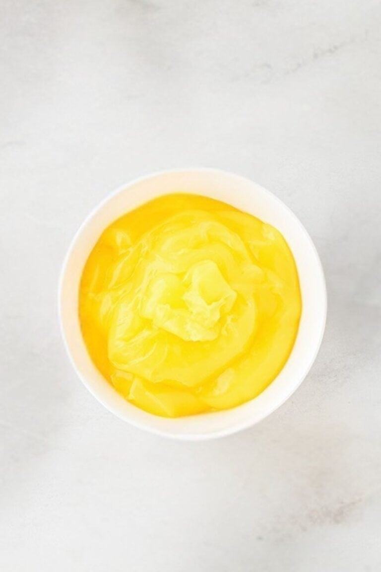 A white bowl filled with smooth yellow custard on a light gray surface.