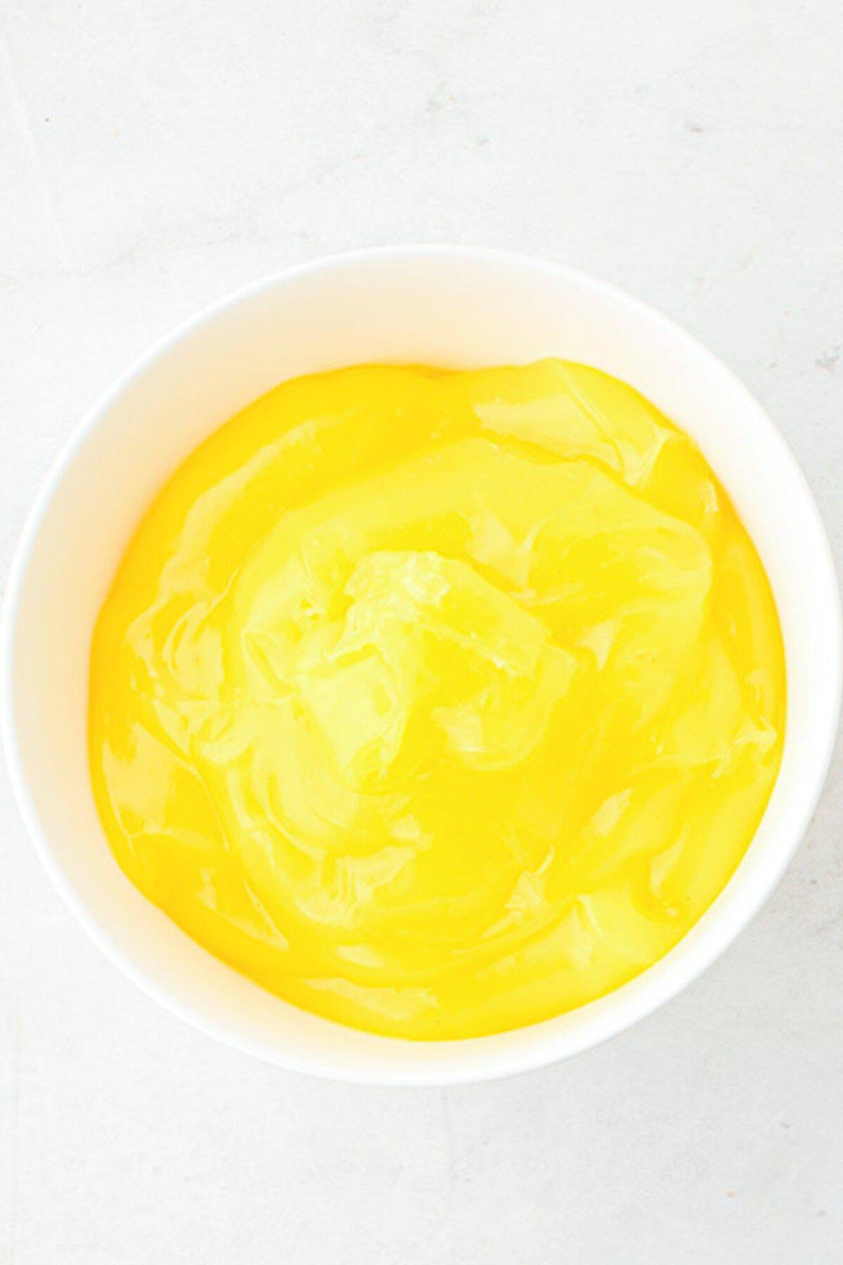 A white bowl filled with smooth, bright yellow pudding on a light-colored surface.