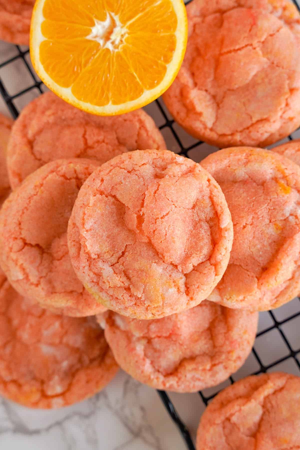 A stack of orange creamsicle cookies sits on a cooling rack next to a halved orange.