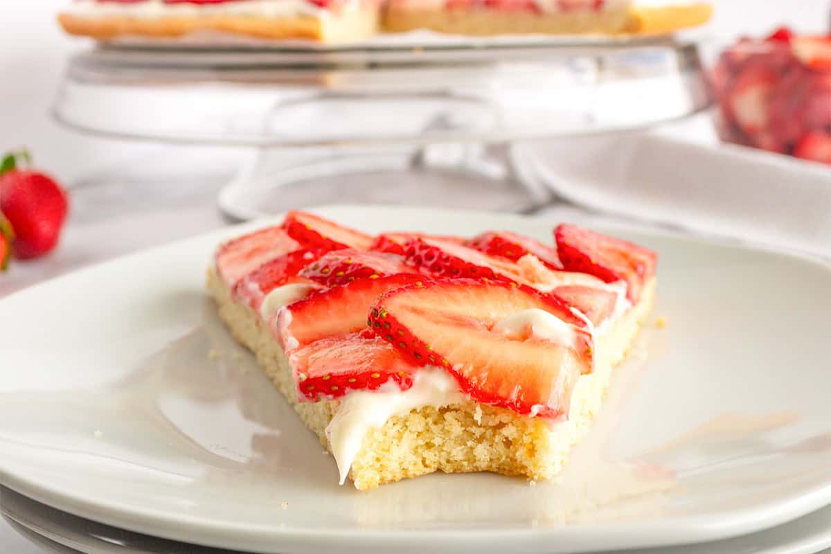 A slice of strawberry tart, reminiscent of a delicious Strawberry Pizza, with a crumbly crust, creamy filling, and fresh strawberry slices on a white plate.