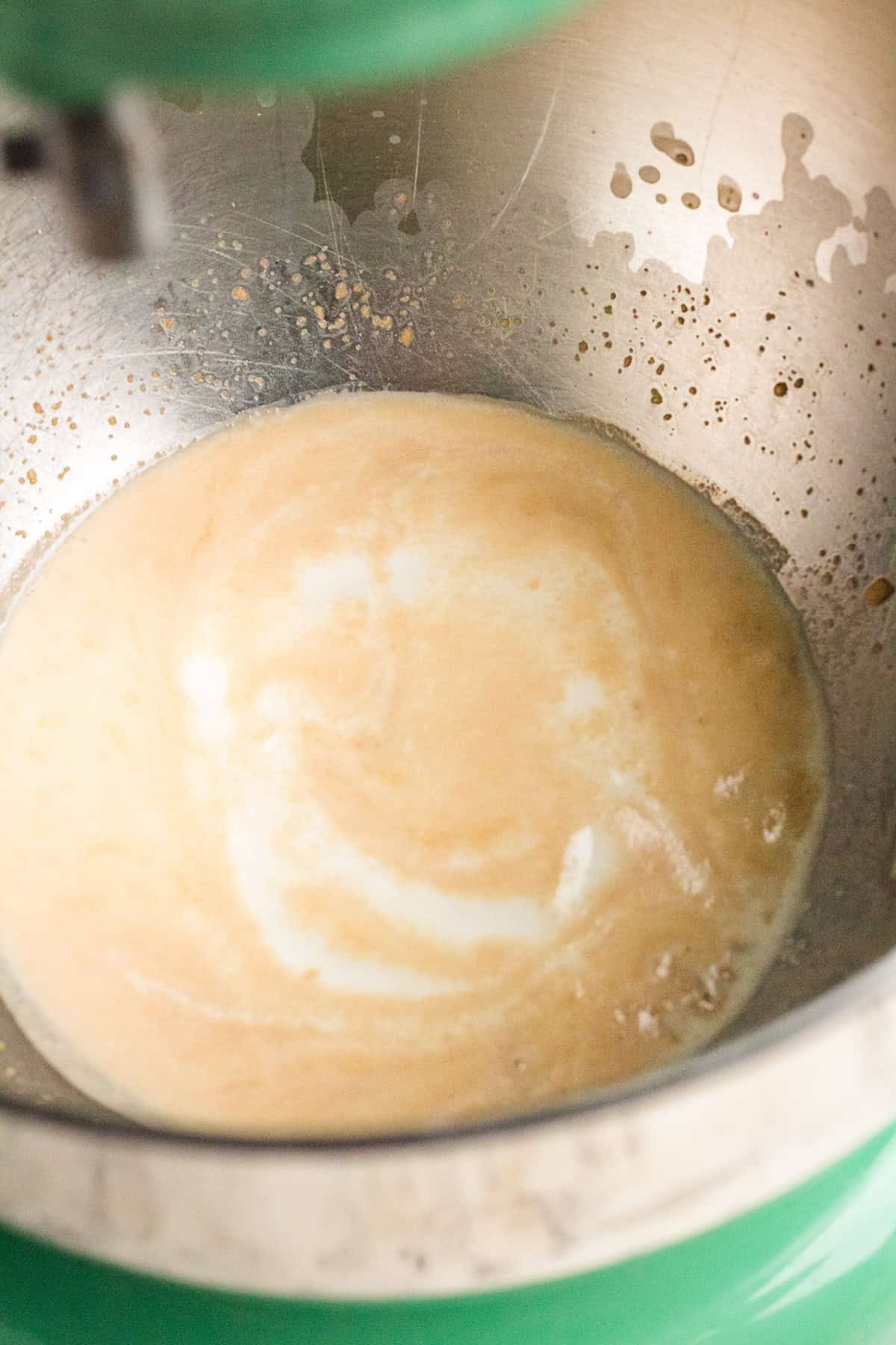 A stand mixer bowl containing a light brown batter or liquid mixture partially blended for Blueberry Swirl Bread.