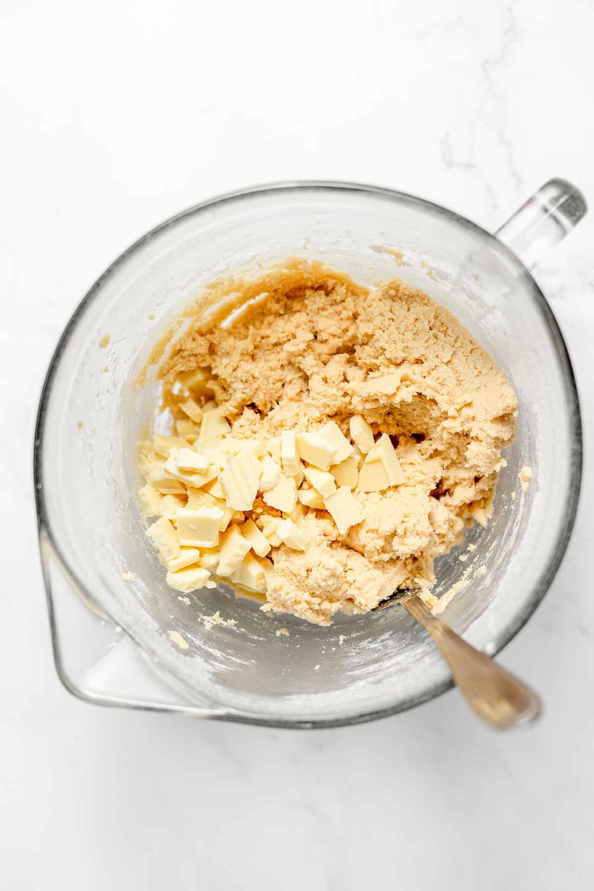 A mixing bowl with cookie dough and chopped white chocolate pieces, perfect for making delicious White Chocolate Cookies, with a metal spoon in the dough.
