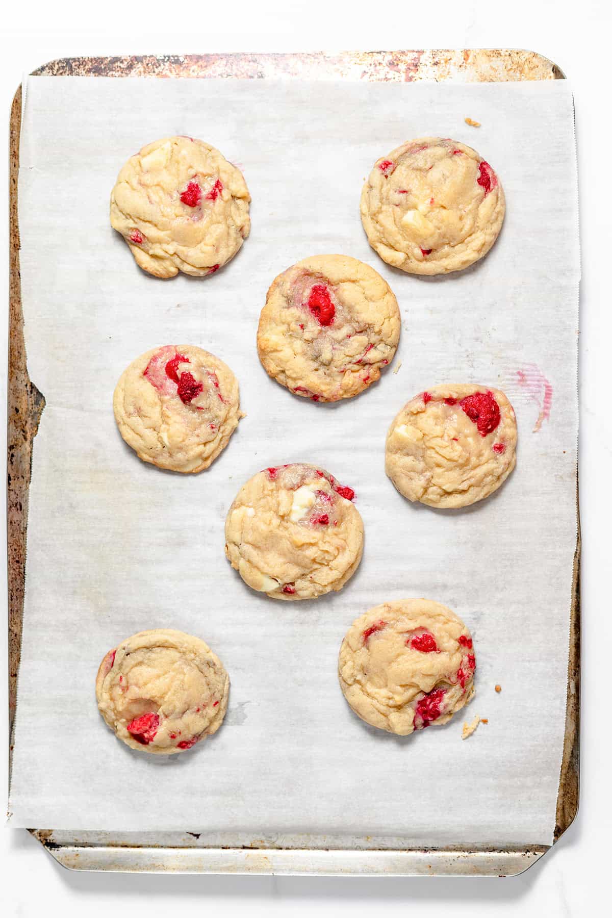 Seven raspberry white chocolate cookies, a delightful blend of White Chocolate Cookies and Raspberry Cookies, are arranged on a baking sheet lined with parchment paper.