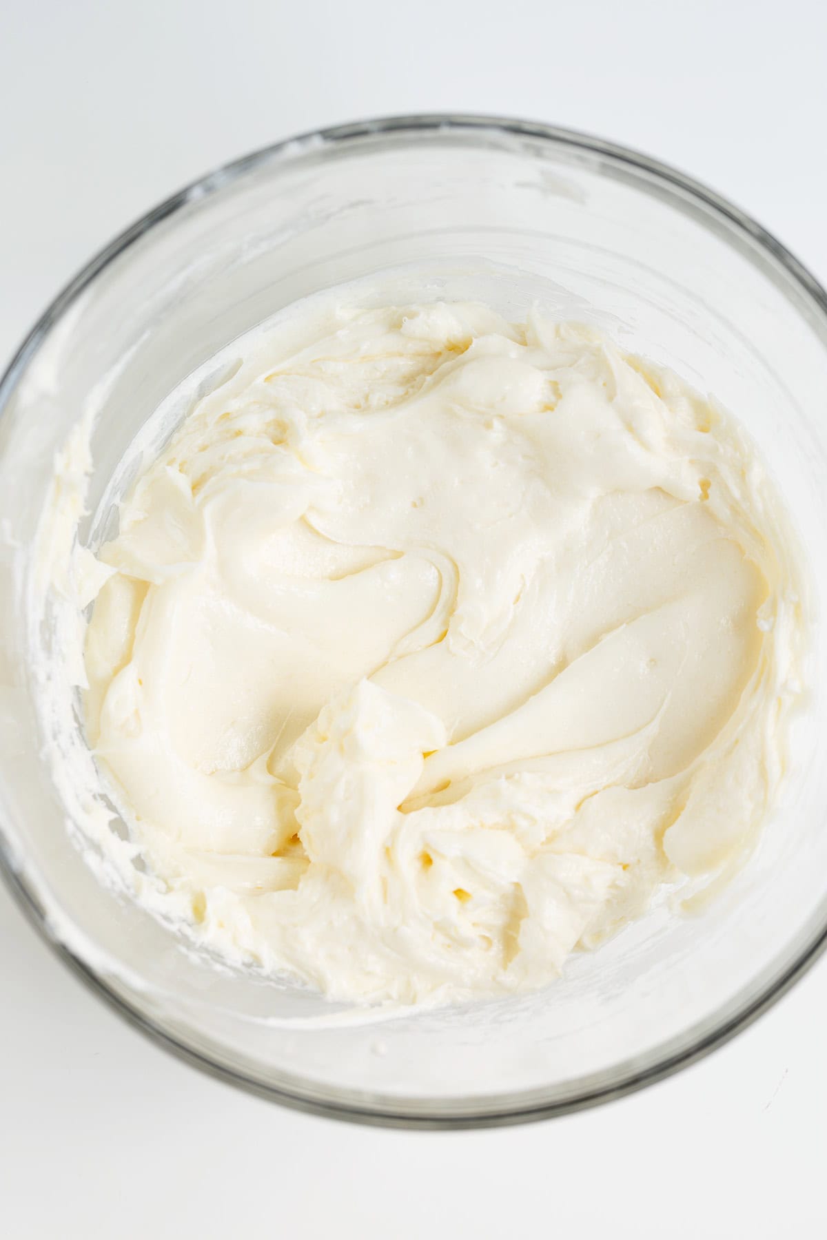 Glass bowl filled with smooth, creamy white Raspberry Cheesecake frosting or batter, shown from above on a white surface.