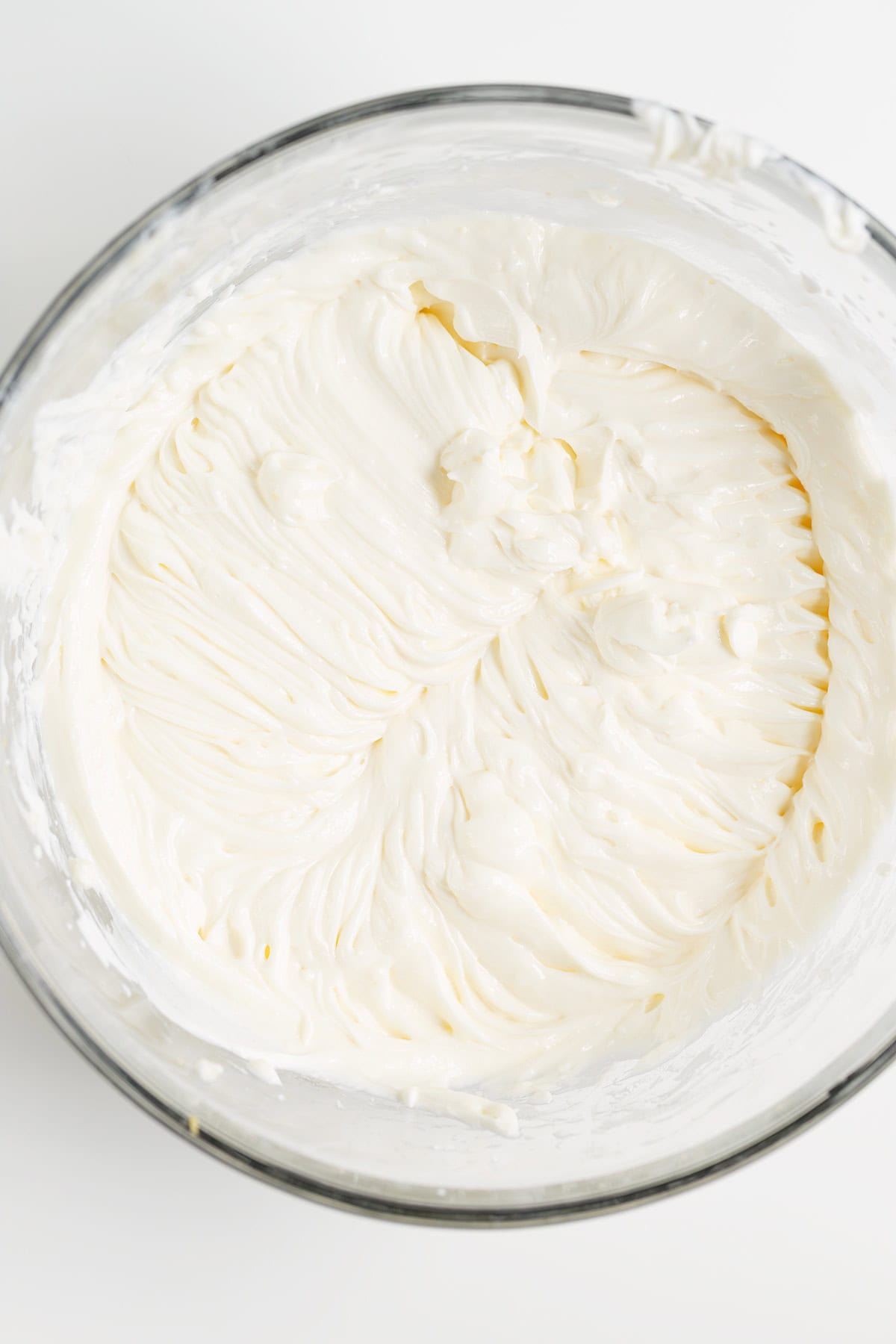 A glass bowl filled with a smooth, whipped raspberry cheesecake cream cheese mixture, showing visible mixing lines on the surface.