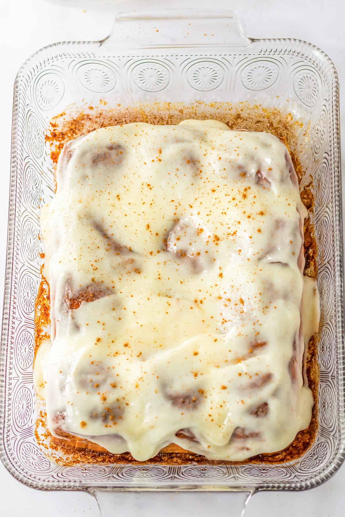 A rectangular glass baking dish with frosted Hawaiian Roll Cinnamon Rolls topped with a creamy white icing and a sprinkle of spice.