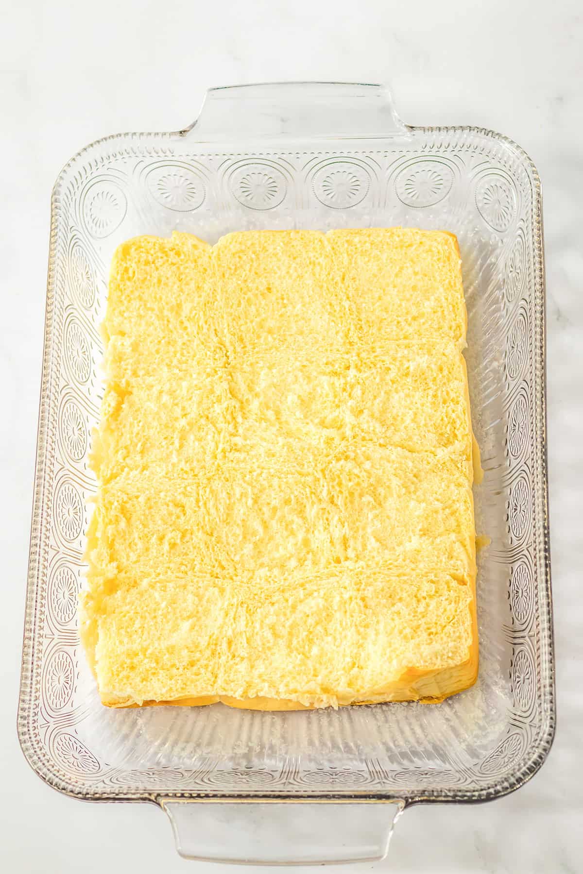 Rectangular glass baking dish with six soft, plain Hawaiian rolls arranged in a single layer on the bottom.