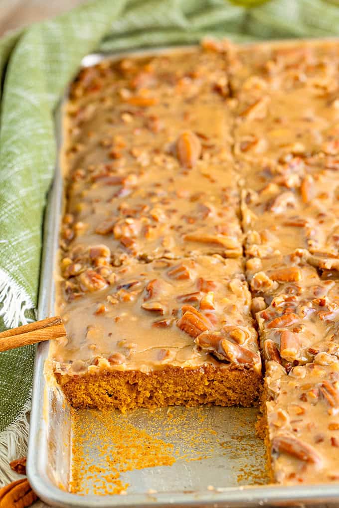 A rectangular pan of pumpkin sheet cake topped with a rich praline icing and pecan glaze, partially sliced with one piece missing.