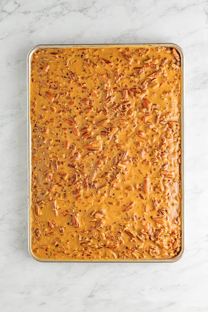 A baking sheet filled with a flat layer of caramel-colored praline icing mixture sits on a white marble surface, perfect for spreading over your favorite pumpkin sheet cake.