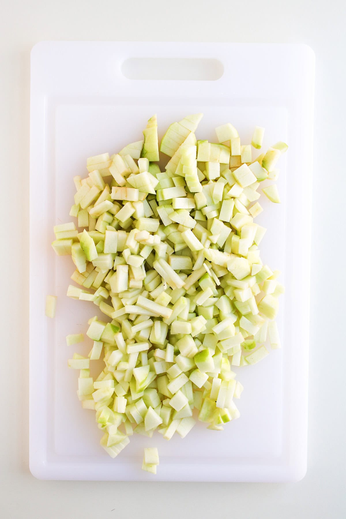 Diced chayote pieces spread on a white plastic cutting board, viewed from above—perfect for pairing with a cream cheese apple dip or as a unique twist in your next cream cheese dessert.