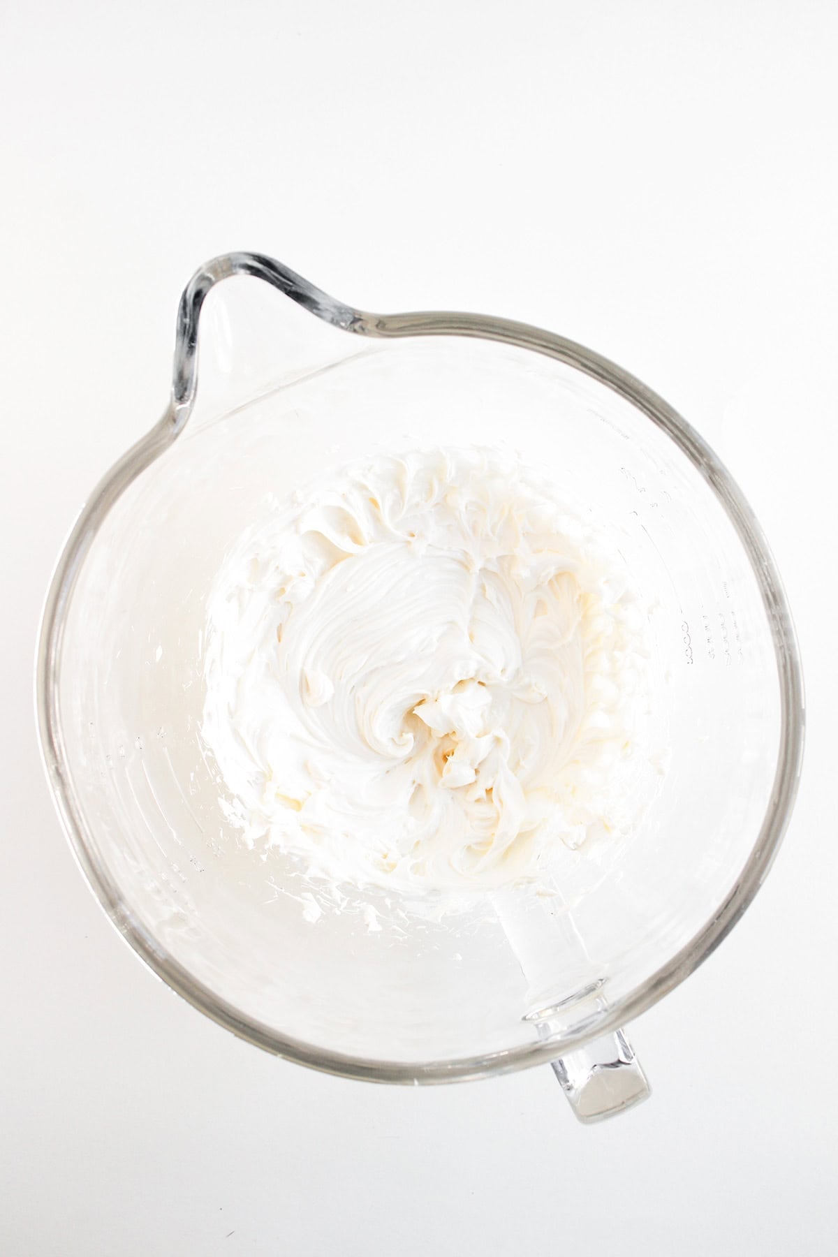 Clear glass mixing bowl containing fluffy, white whipped mixture—perfect for a dessert dip like apple pie dip with cream cheese—viewed from above on a plain white background.