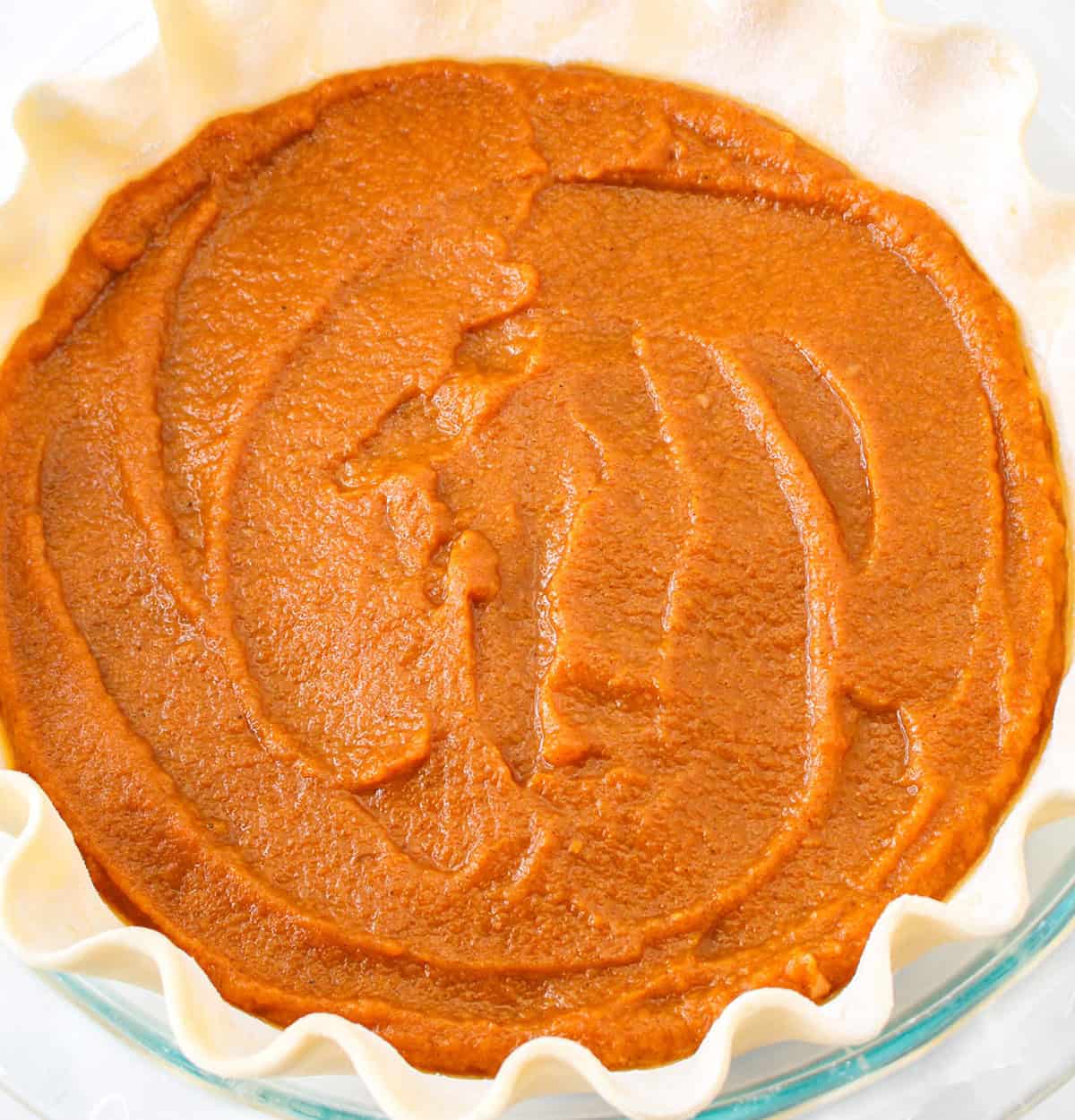 Unbaked Pumpkin Pie filling spread evenly in a pie crust with fluted edges, ready to go in the oven—perfect for those who love the creamy richness of pumpkin desserts or crave classic holiday flavors like Pecan Pie.