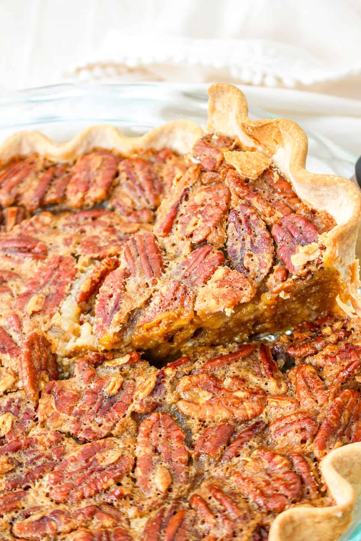 A close-up of a Pecan Pie with one slice being lifted, showing a flaky crust and a rich filling topped with whole pecans—perfect for anyone deciding between classic Pumpkin Pie or nutty holiday treats.