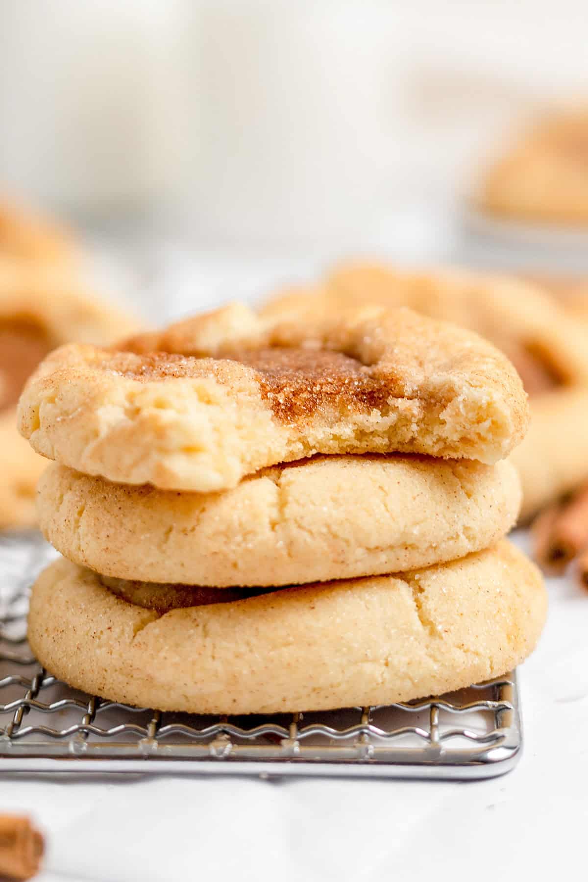 A stack of three cinnamon snickerdoodle cookies on a wire cooling rack, with a bite taken out of the top cookie.