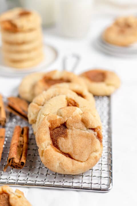 Freshly baked snickerdoodle cookies on a wire cooling rack next to cinnamon sticks.