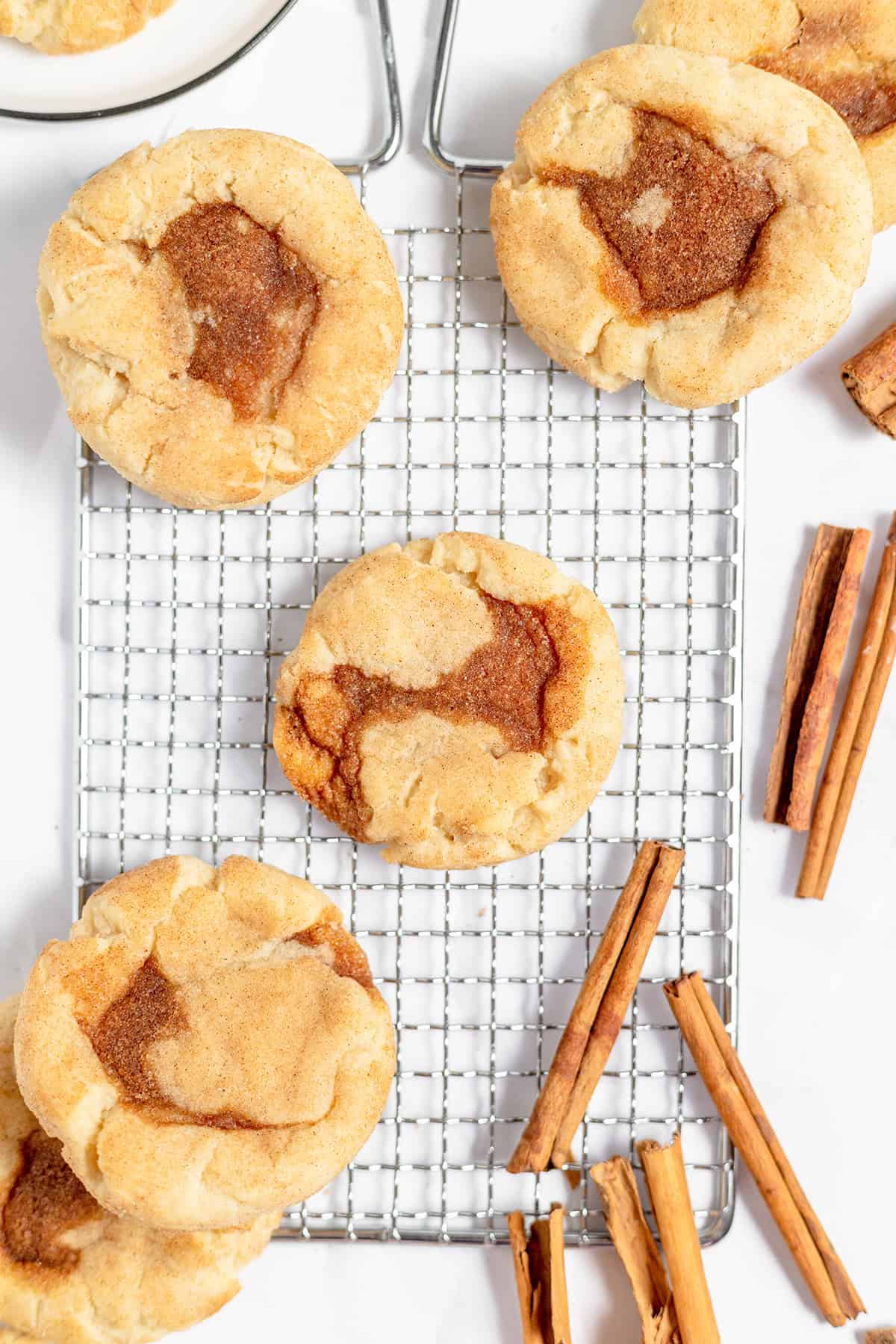 Snickerdoodle cinnamon roll cookies on a wire cooling rack, surrounded by cinnamon sticks.