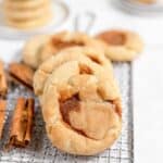 A row of cinnamon sugar snickerdoodles on a wire cooling rack with cinnamon sticks nearby.