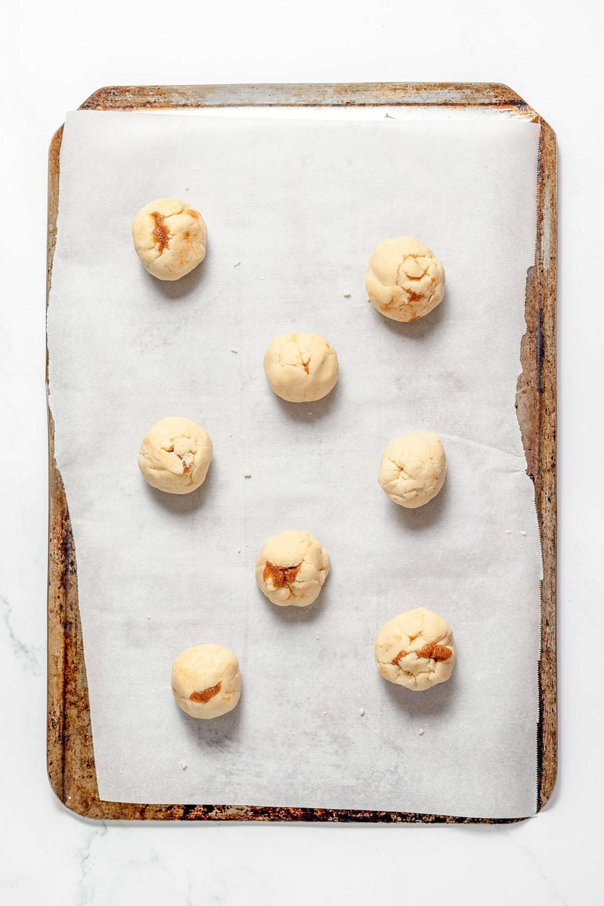 Seven round balls of cinnamon roll snickerdoodle dough spaced out on a parchment-lined baking sheet.