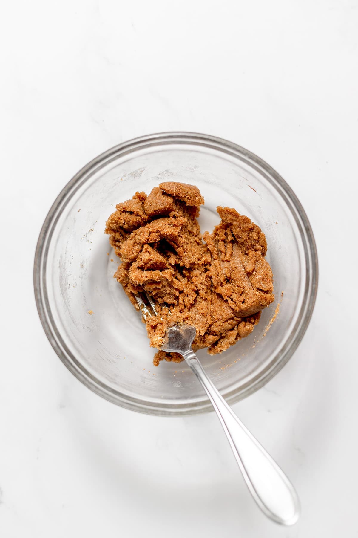A glass bowl containing a thick, brown mixture for snickerdoodle cookies being stirred with a metal fork.