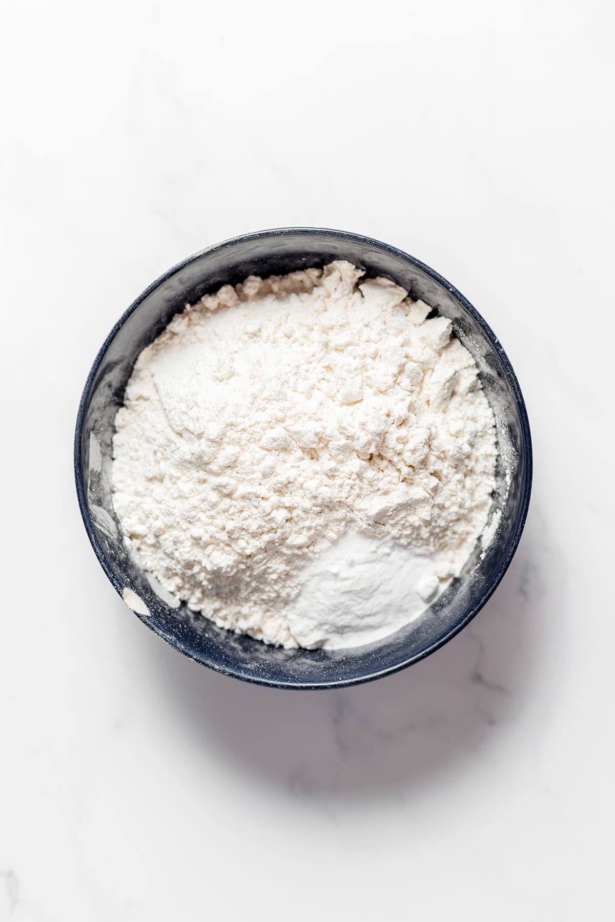 A bowl filled with flour and a small mound of baking powder for cinnamon roll cookies.