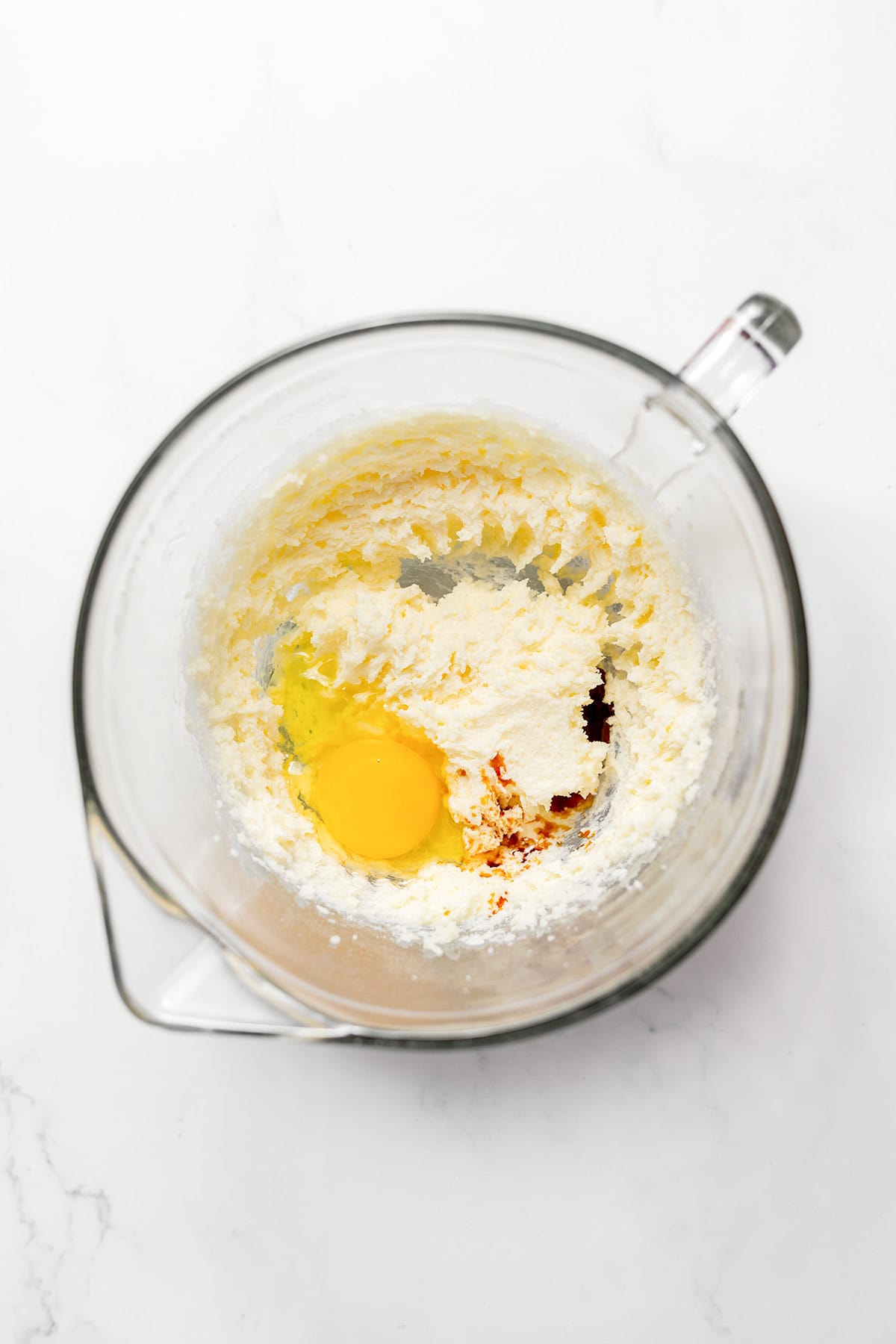 A raw egg and a splash of vanilla extract in a glass mixing bowl with creamed butter and sugar for snickerdoodles.