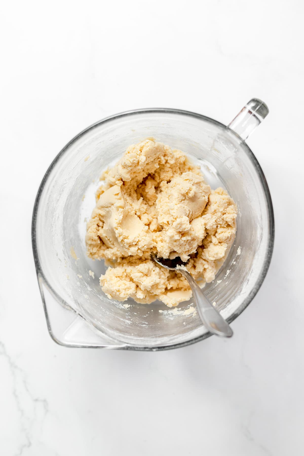 A metal spoon rests in a glass mixing bowl containing a ball of raw snickerdoodle cookie dough.