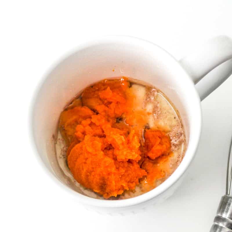 Mashed pumpkin and liquid ingredients mixed together in a white mug for a pumpkin mug cake.