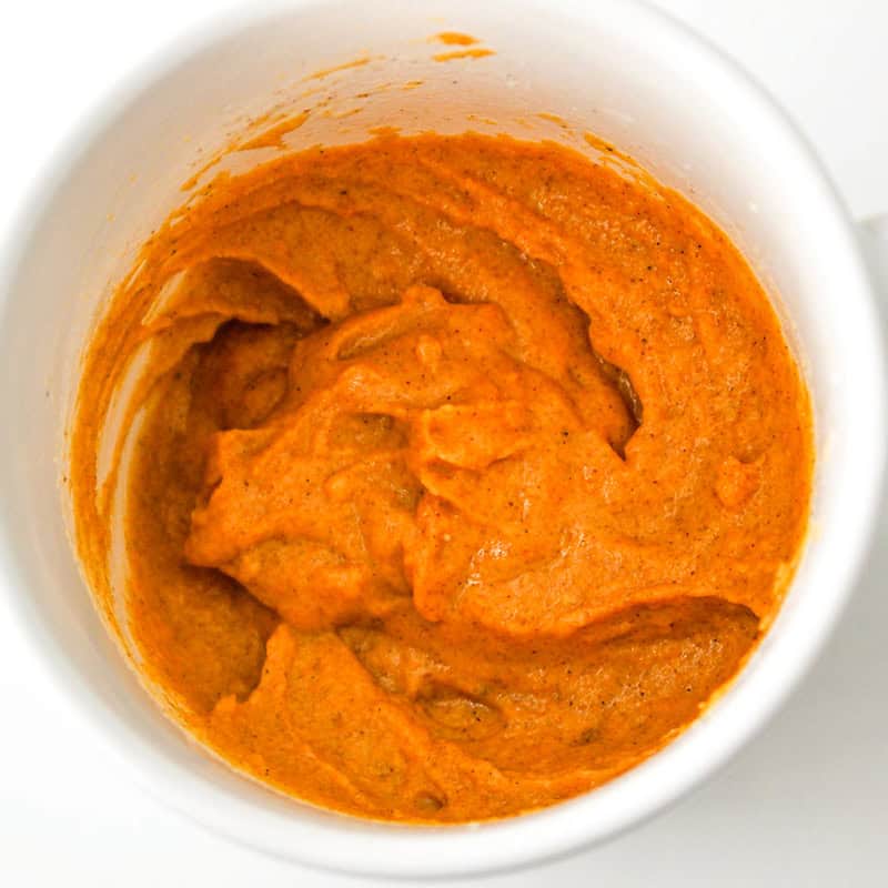 A white mug filled with a thick, orange-colored pumpkin mug cake.