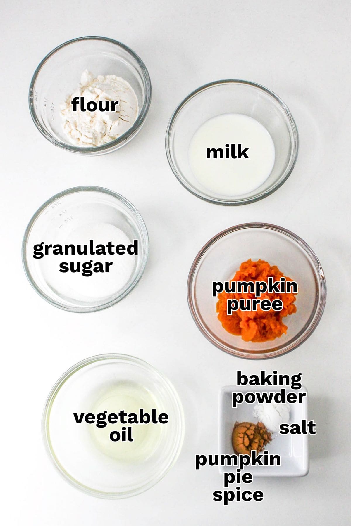 Top-down view of ingredient bowls for a pumpkin mug cake, including flour, milk, sugar, pumpkin puree, oil, baking powder, salt, and spice.