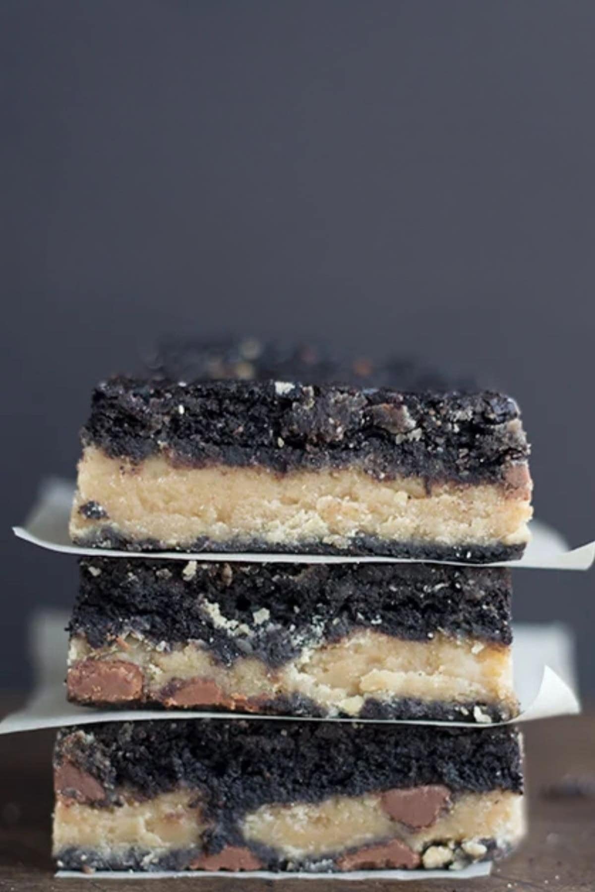 A stack of three layered peanut butter fudge brownies with dark brown cookie crusts, a light tan filling, and chocolate chips.