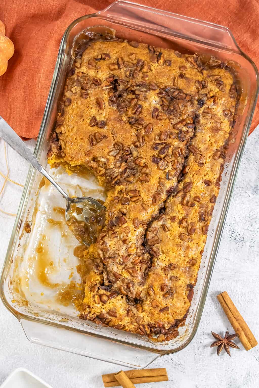 A rectangular glass baking dish filled with a baked pecan pudding cake, with a serving spoon resting in the dish.