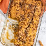 A rectangular glass baking dish filled with a baked pecan pudding cake, with a serving spoon resting in the dish.