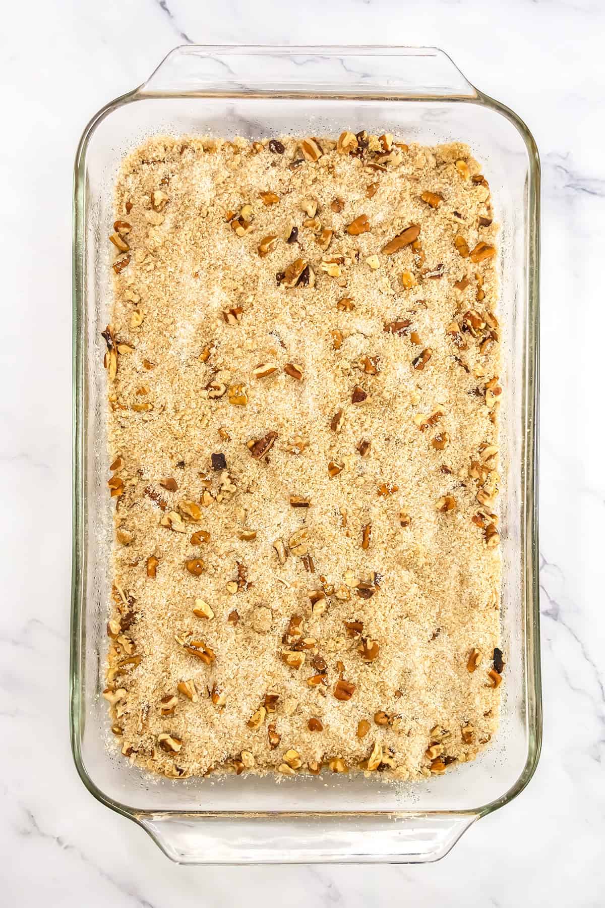 A rectangular glass baking dish filled with a pumpkin pecan pudding cake crumble topping mixed with chopped nuts.