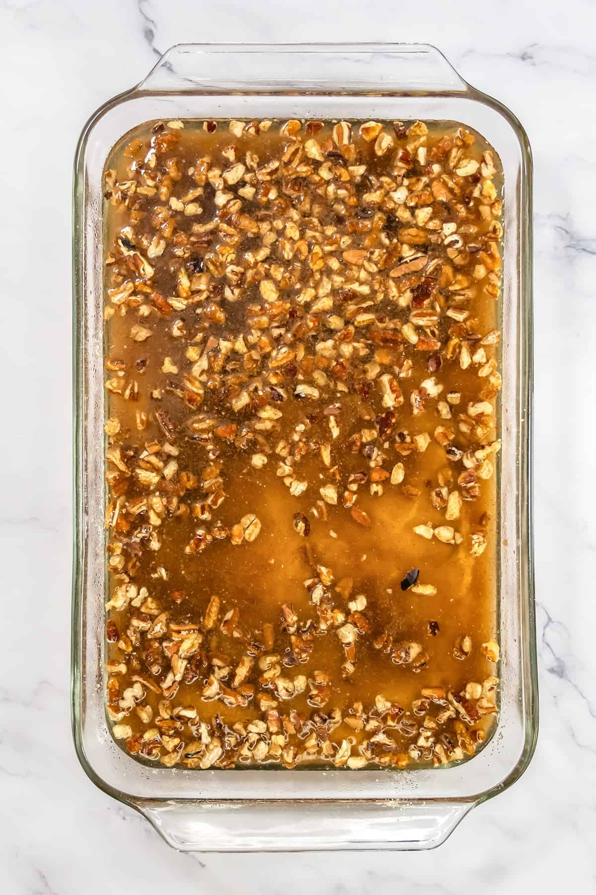 Chopped pecans in a syrup mixture in a glass baking dish, prepared for a pumpkin pecan dessert.