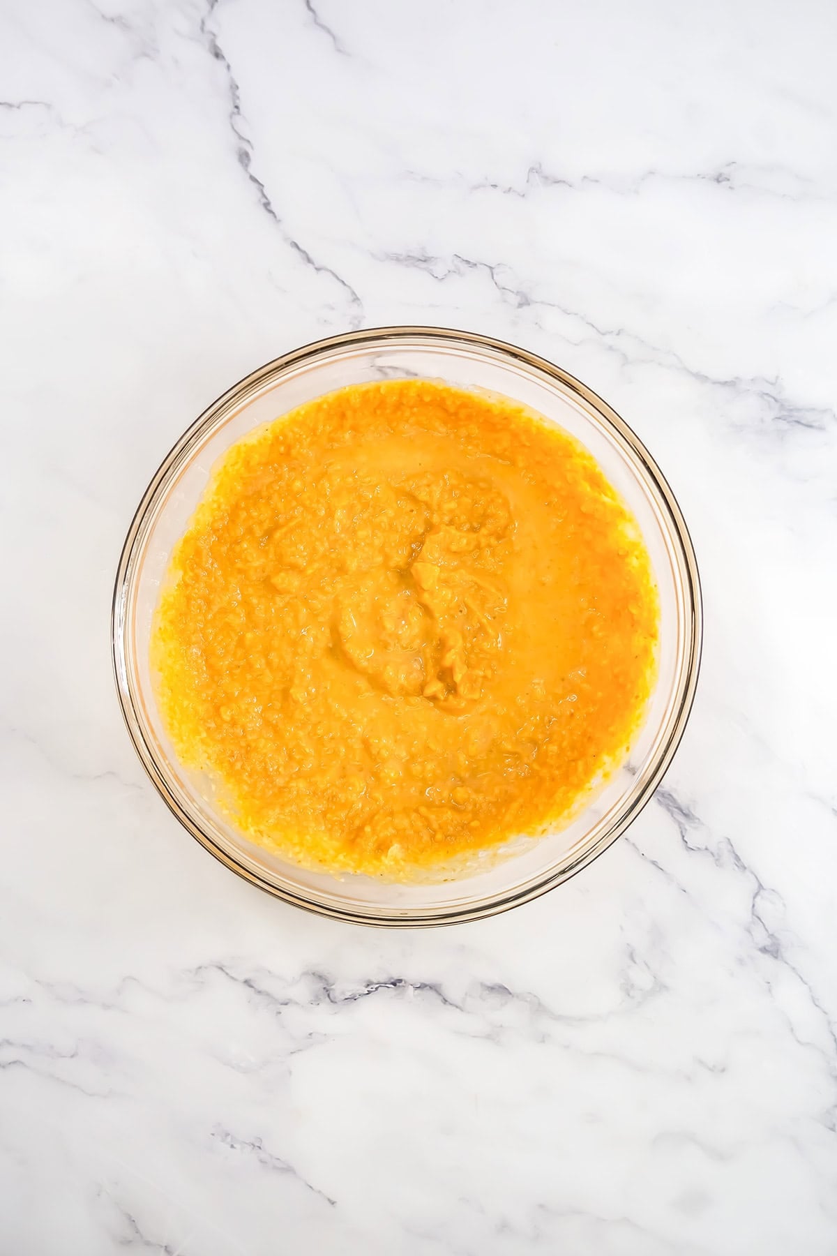 A glass bowl of pumpkin pudding cake purée on a white marble surface.